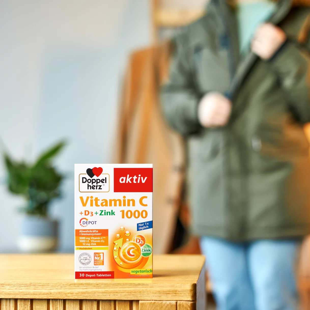 Doppelherz Vitamin C 1000 auf Kommode mit Frau im Hintergrund